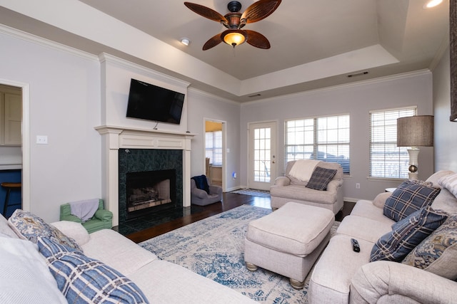 living room with a premium fireplace, wood finished floors, visible vents, ornamental molding, and a tray ceiling