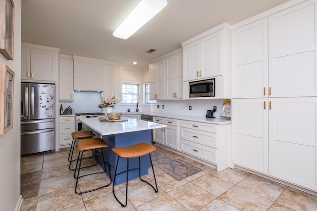 kitchen with light countertops, backsplash, appliances with stainless steel finishes, a kitchen island, and a kitchen bar