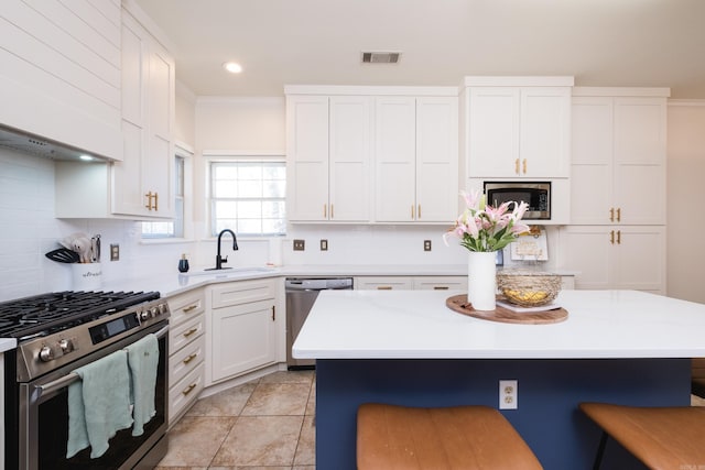 kitchen featuring visible vents, appliances with stainless steel finishes, a sink, wall chimney range hood, and a kitchen breakfast bar