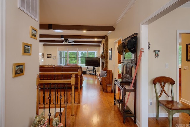 hallway featuring wood finished floors, visible vents, baseboards, beamed ceiling, and crown molding