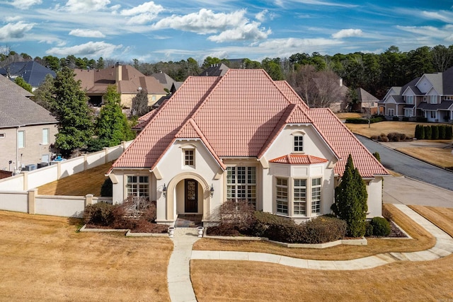 view of front facade featuring a tiled roof, fence, a residential view, and stucco siding