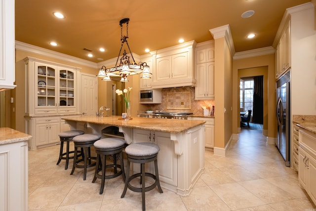 kitchen with built in appliances, a kitchen breakfast bar, ornamental molding, backsplash, and an island with sink