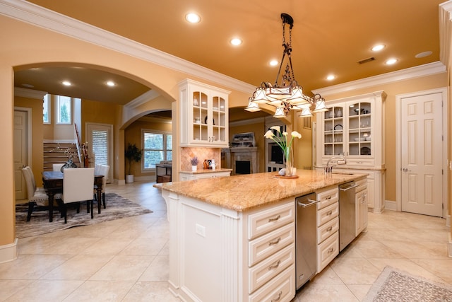 kitchen with light stone counters, arched walkways, visible vents, glass insert cabinets, and a kitchen island with sink