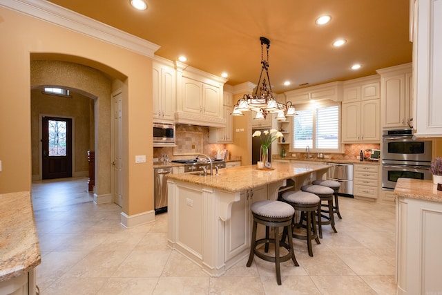 kitchen with arched walkways, a kitchen island with sink, stainless steel appliances, a sink, and recessed lighting