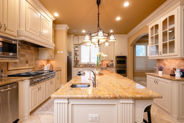 kitchen with a center island with sink, decorative backsplash, glass insert cabinets, a sink, and built in appliances