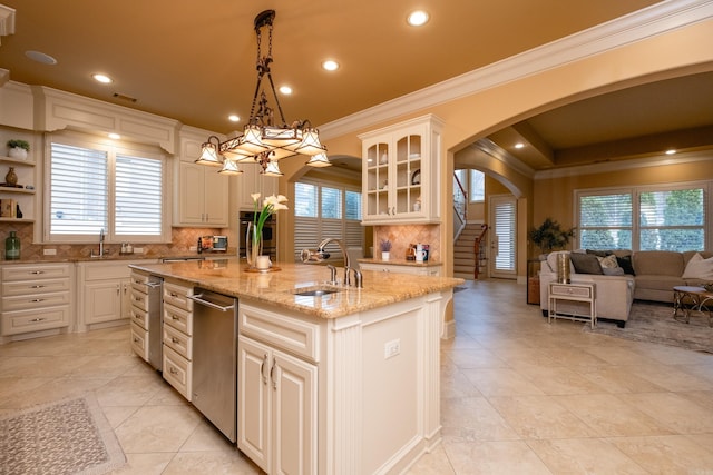 kitchen with arched walkways, crown molding, glass insert cabinets, a kitchen island with sink, and a sink