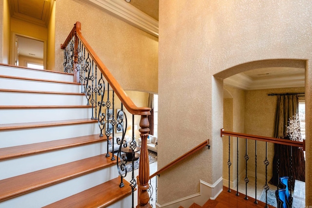 stairs featuring arched walkways, a textured wall, ornamental molding, and baseboards