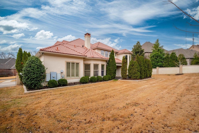 back of house with fence, a tiled roof, a yard, stucco siding, and a chimney