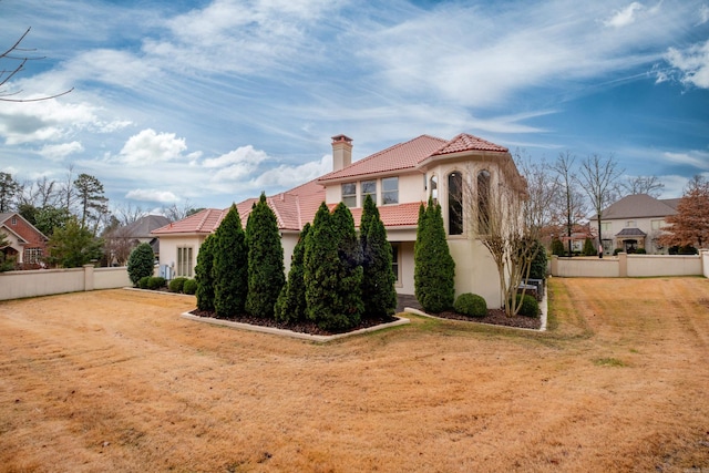 view of front of property featuring stucco siding, a chimney, a tiled roof, fence, and a front yard