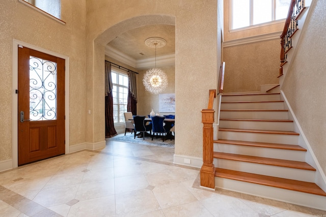 foyer with arched walkways, a notable chandelier, stairway, ornamental molding, and baseboards