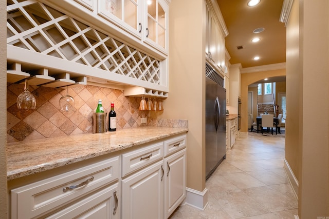 kitchen featuring tasteful backsplash, arched walkways, glass insert cabinets, stainless steel built in refrigerator, and crown molding