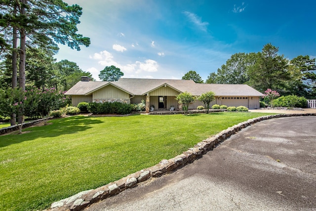 ranch-style home featuring a front yard, driveway, a chimney, and an attached garage