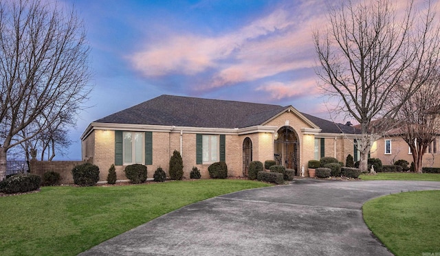 ranch-style house with a shingled roof, brick siding, a lawn, and driveway