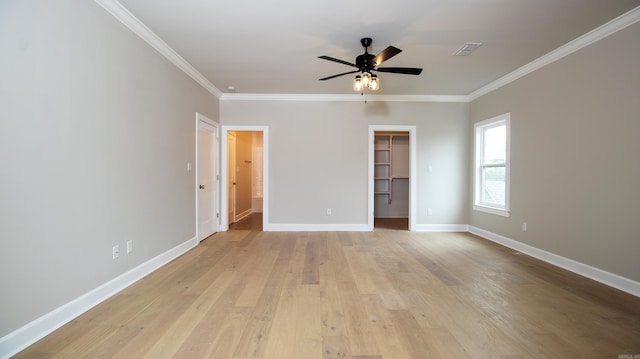 unfurnished bedroom with baseboards, visible vents, ornamental molding, a walk in closet, and light wood-type flooring