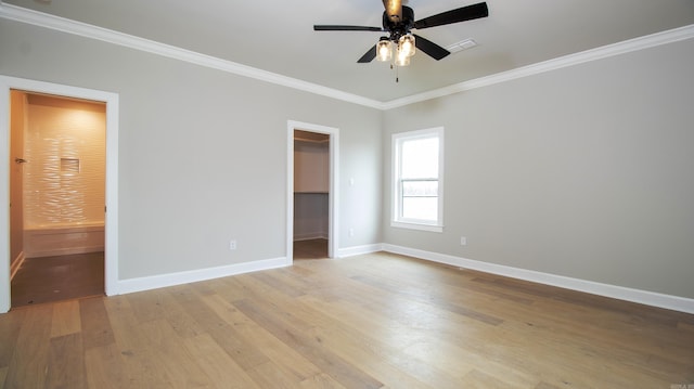 unfurnished bedroom with a walk in closet, light wood finished floors, visible vents, ornamental molding, and baseboards