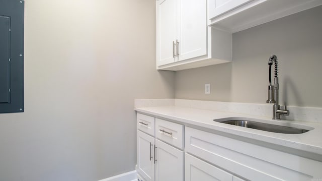 kitchen featuring white cabinetry, a sink, light stone countertops, electric panel, and baseboards