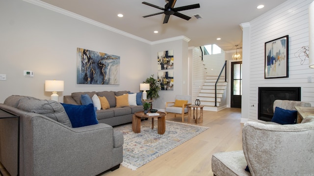 living area with a fireplace, visible vents, light wood-style floors, stairway, and crown molding