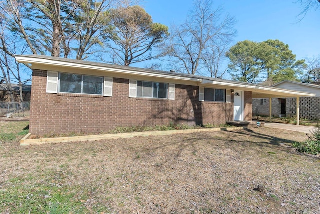 single story home featuring brick siding, a front yard, fence, a carport, and driveway