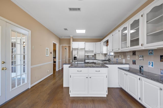 kitchen with visible vents, glass insert cabinets, a sink, dark stone countertops, and stainless steel fridge with ice dispenser