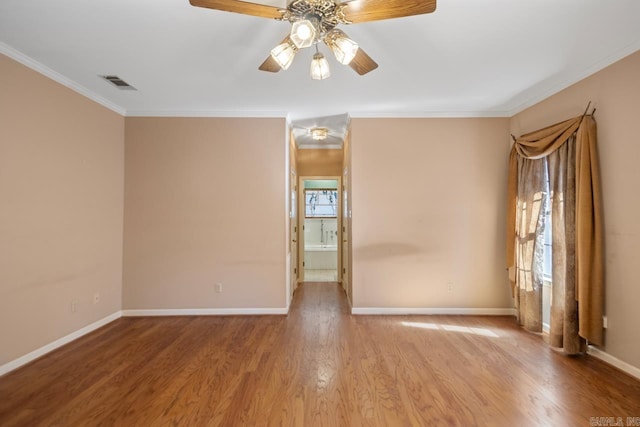 empty room featuring visible vents, crown molding, baseboards, and wood finished floors