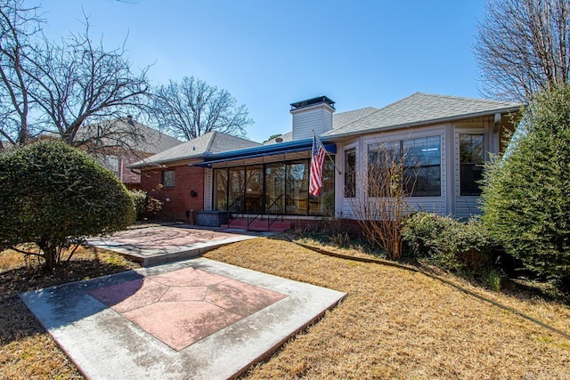 back of property with brick siding, a yard, a patio, a chimney, and a sunroom