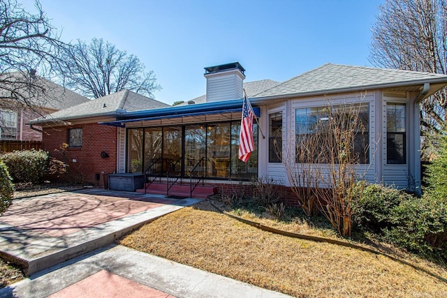 rear view of property with brick siding, a chimney, a shingled roof, and a sunroom