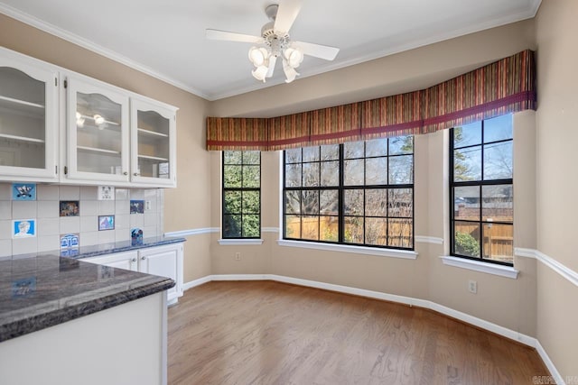 unfurnished dining area featuring a ceiling fan, light wood-style flooring, ornamental molding, and baseboards