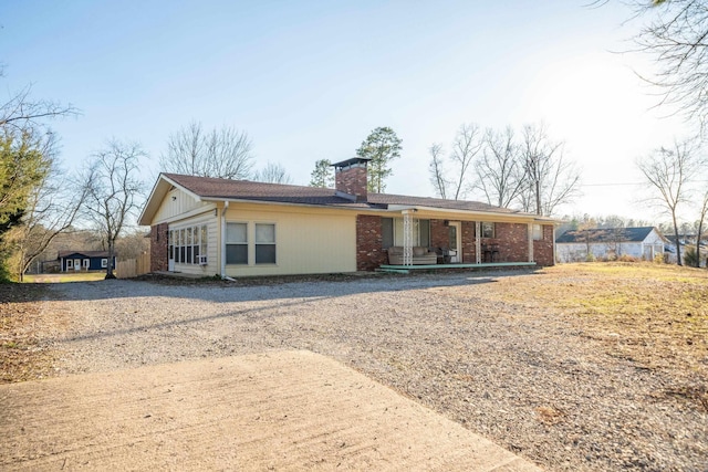 view of front facade with covered porch, a chimney, and brick siding