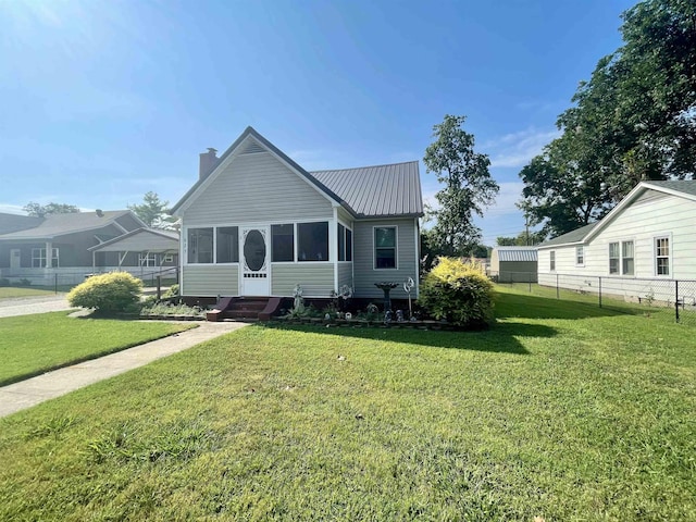 view of front of house with a chimney, a sunroom, metal roof, fence, and a front lawn