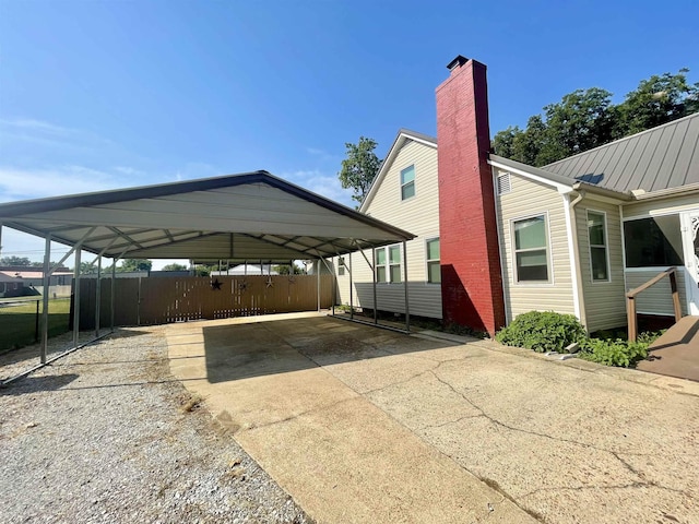 exterior space featuring metal roof, fence, concrete driveway, a detached carport, and a chimney