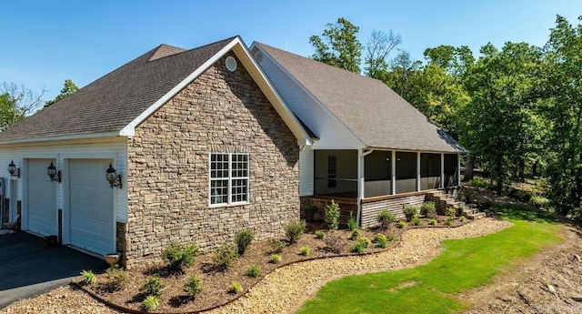 view of home's exterior with stone siding, a detached garage, and a sunroom