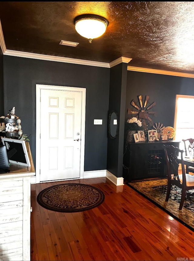 foyer entrance with a textured ceiling, ornamental molding, wood finished floors, and baseboards