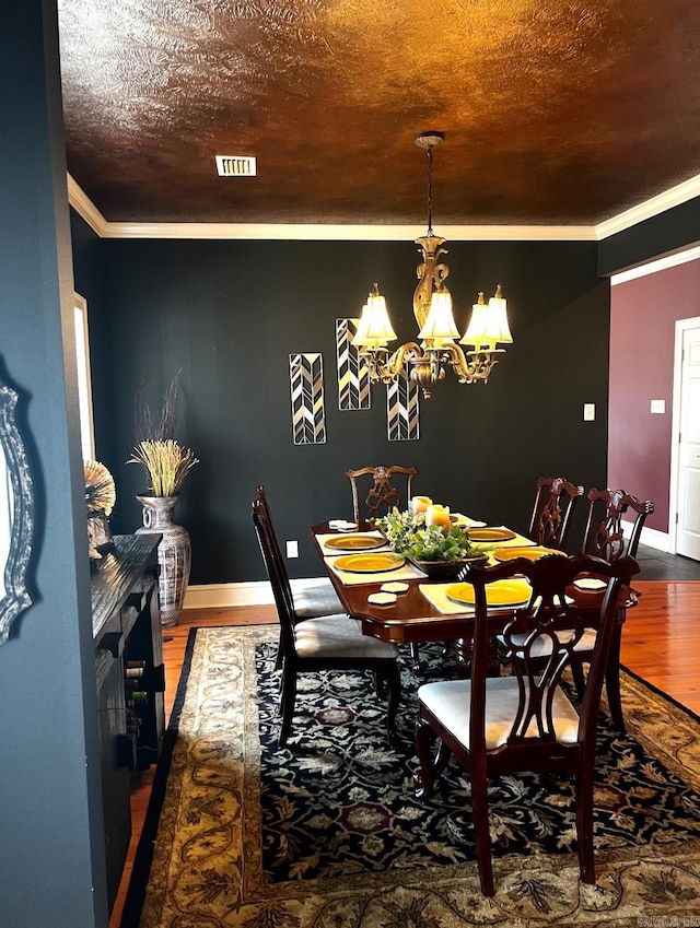 dining area with baseboards, visible vents, wood finished floors, crown molding, and a chandelier