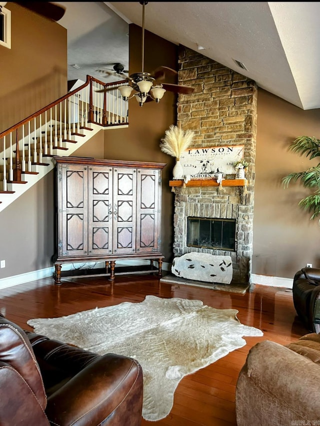 living area with baseboards, ceiling fan, wood finished floors, stairs, and a stone fireplace