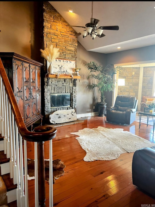 living room with hardwood / wood-style flooring, ceiling fan, stairs, vaulted ceiling, and a stone fireplace