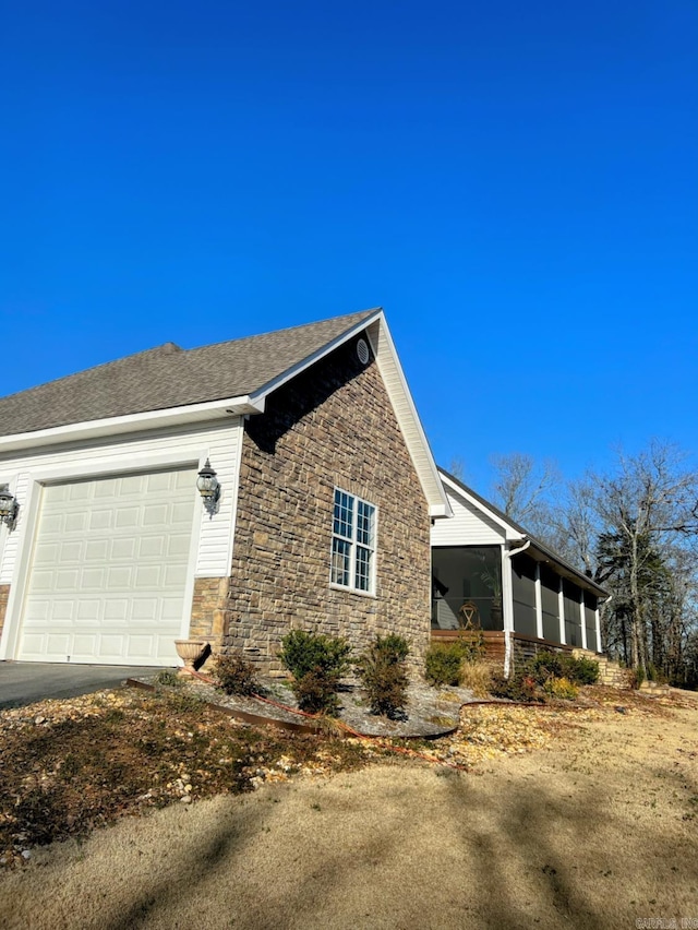 view of home's exterior featuring a garage, stone siding, a shingled roof, and a sunroom