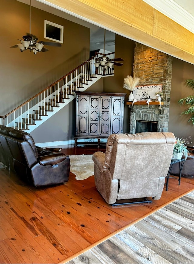 living room featuring a ceiling fan, wood-type flooring, stairs, a fireplace, and high vaulted ceiling