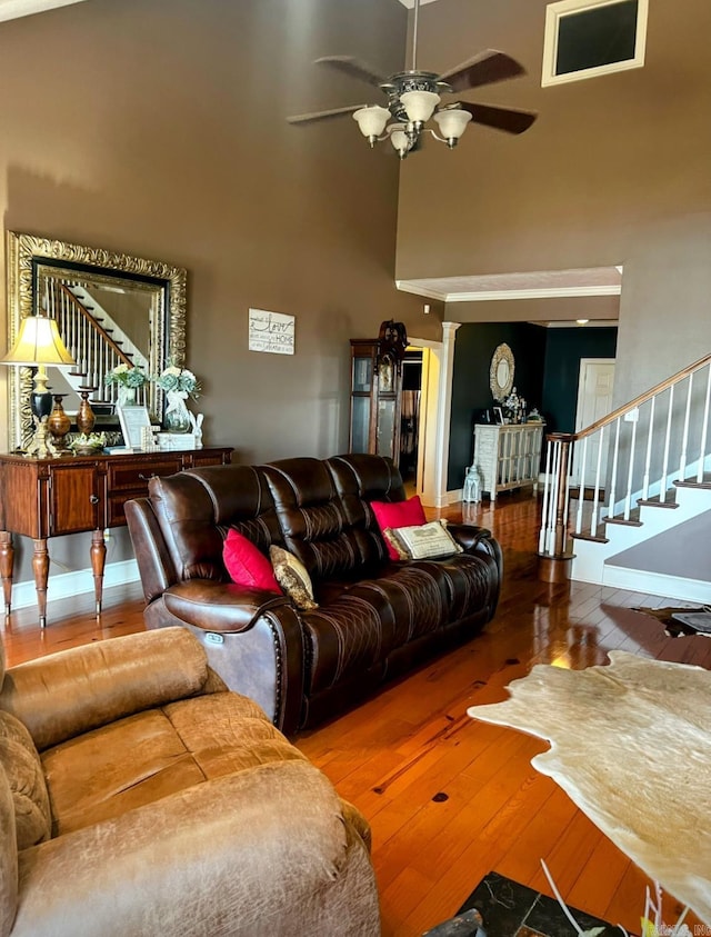 living area featuring a towering ceiling, baseboards, stairs, a ceiling fan, and wood-type flooring