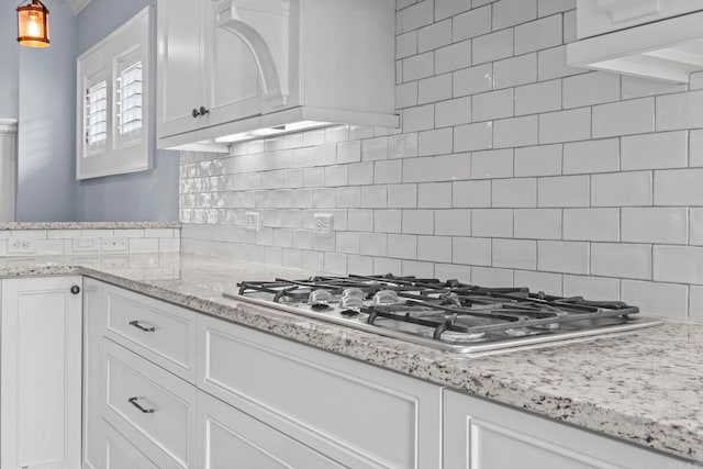 kitchen with tasteful backsplash, white cabinets, light stone countertops, under cabinet range hood, and stainless steel gas cooktop