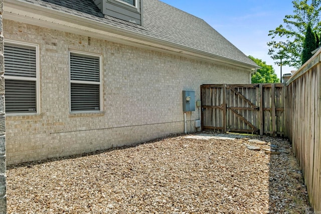 view of side of property with a gate, roof with shingles, and fence