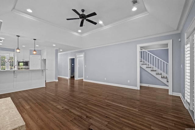 unfurnished living room with a tray ceiling, dark wood-style flooring, visible vents, and ceiling fan with notable chandelier