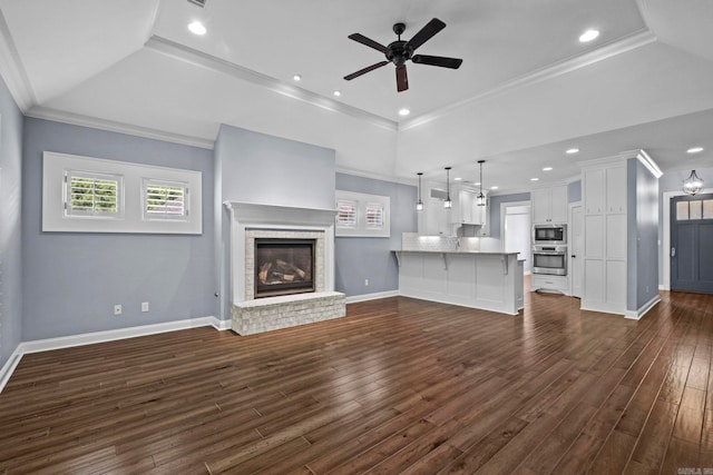 unfurnished living room featuring ornamental molding, dark wood-style flooring, a fireplace, and a raised ceiling