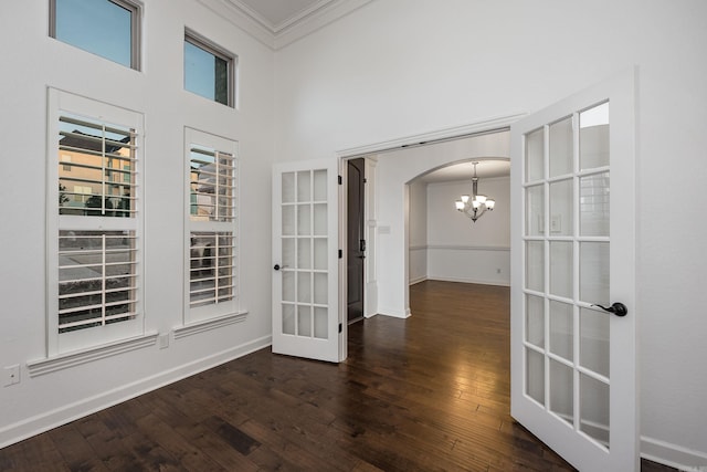 corridor featuring arched walkways, french doors, a notable chandelier, wood-type flooring, and ornamental molding