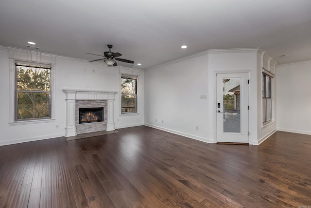 unfurnished living room with ornamental molding, a stone fireplace, dark wood finished floors, and a wealth of natural light