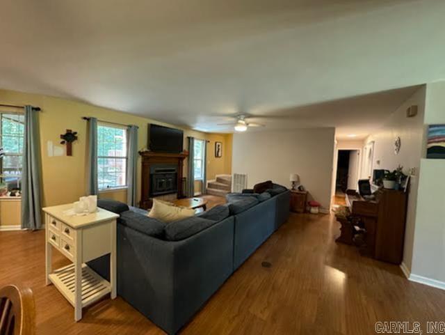 living area with a ceiling fan, a fireplace, baseboards, and wood finished floors