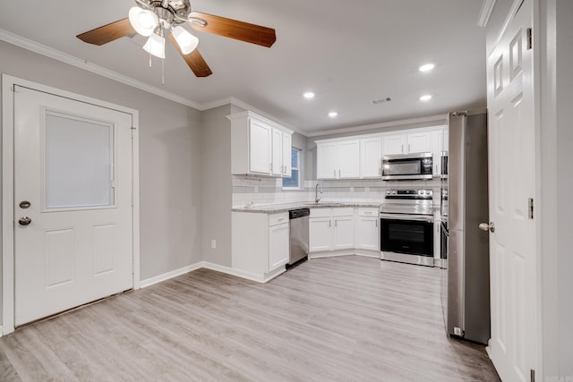 kitchen with stainless steel appliances, a sink, ornamental molding, light wood-type flooring, and tasteful backsplash