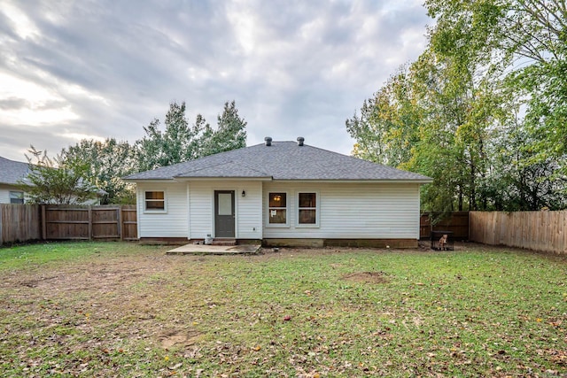 rear view of house with roof with shingles, a lawn, and a fenced backyard