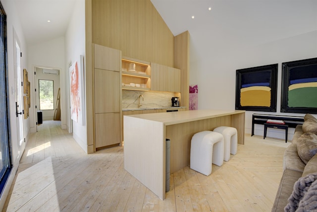 kitchen featuring tasteful backsplash, modern cabinets, light wood-style floors, light brown cabinets, and high vaulted ceiling