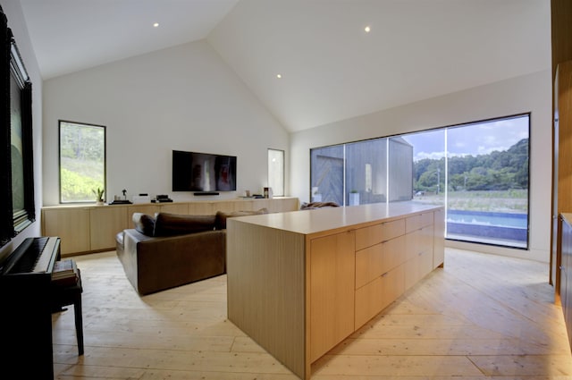 kitchen with modern cabinets, open floor plan, light wood-style floors, light brown cabinets, and high vaulted ceiling