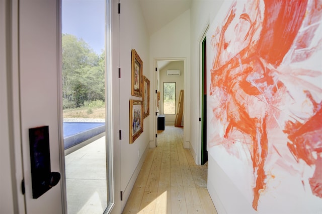 hallway with light wood-type flooring, a wall unit AC, baseboards, and vaulted ceiling